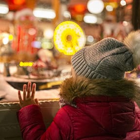 Young child in winter coat looking through store window at toys