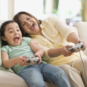 Hispanic mother and daughter leaning back on a couch using controllers to play a video game