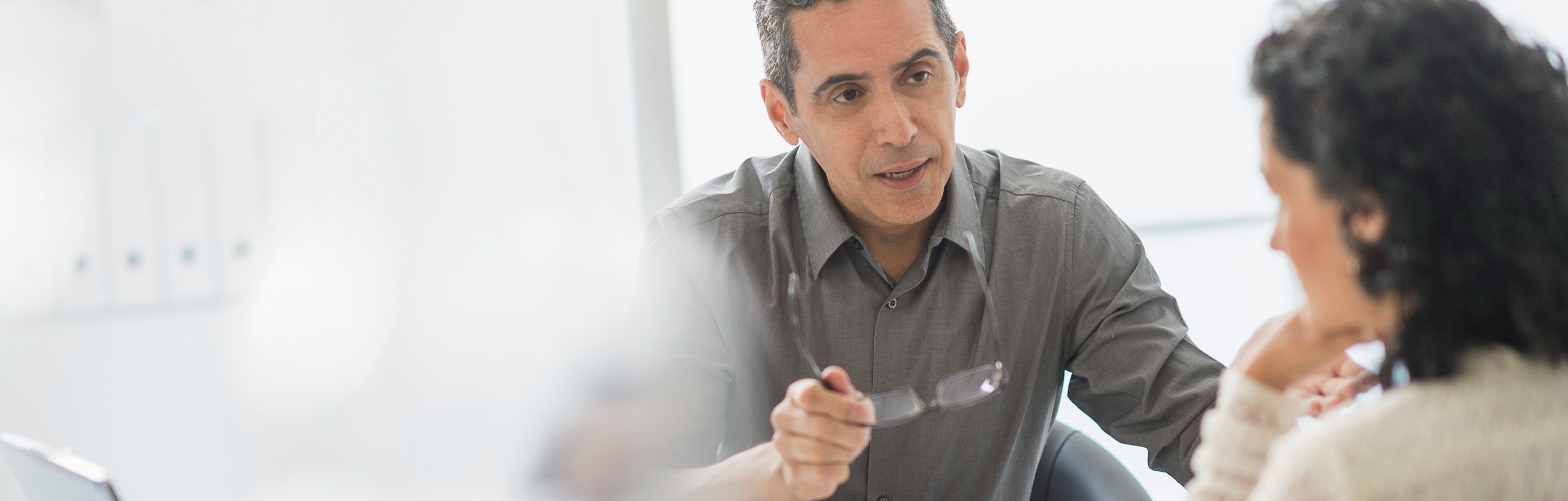 Man holding his glasses and seriously explaining something to a woman