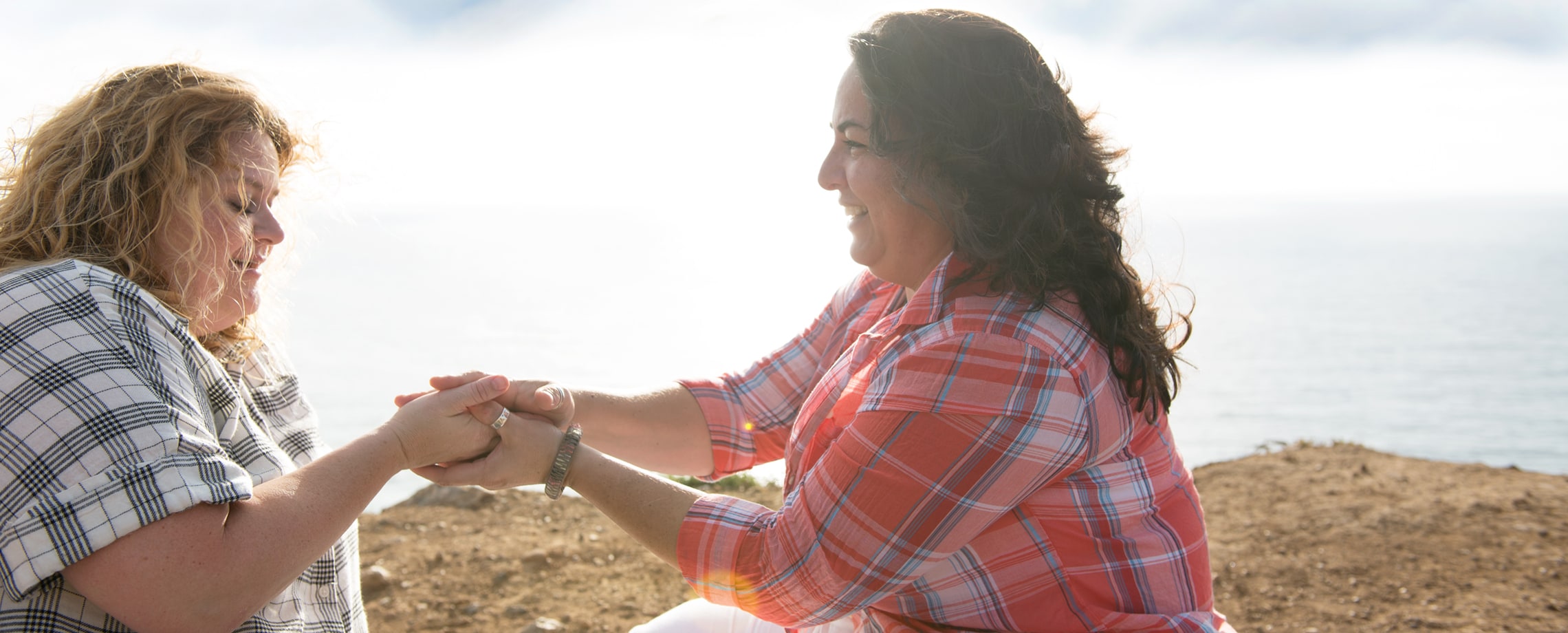 Two Caucasian females sitting on the ground holding hands and smiling