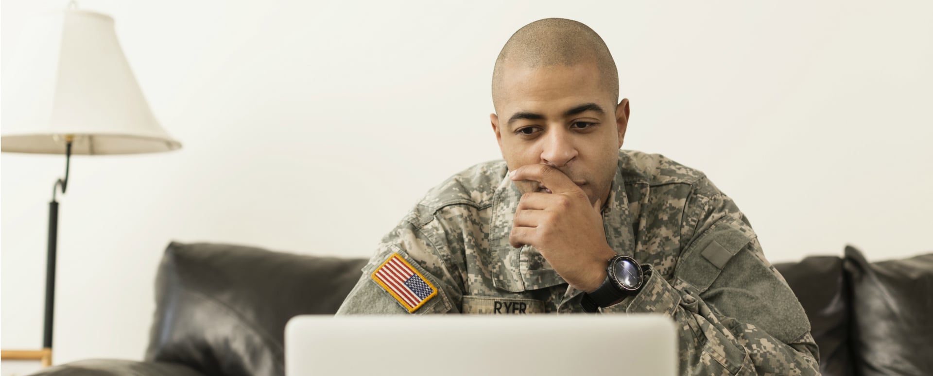 African-American male soldier in uniform at home looking on laptop