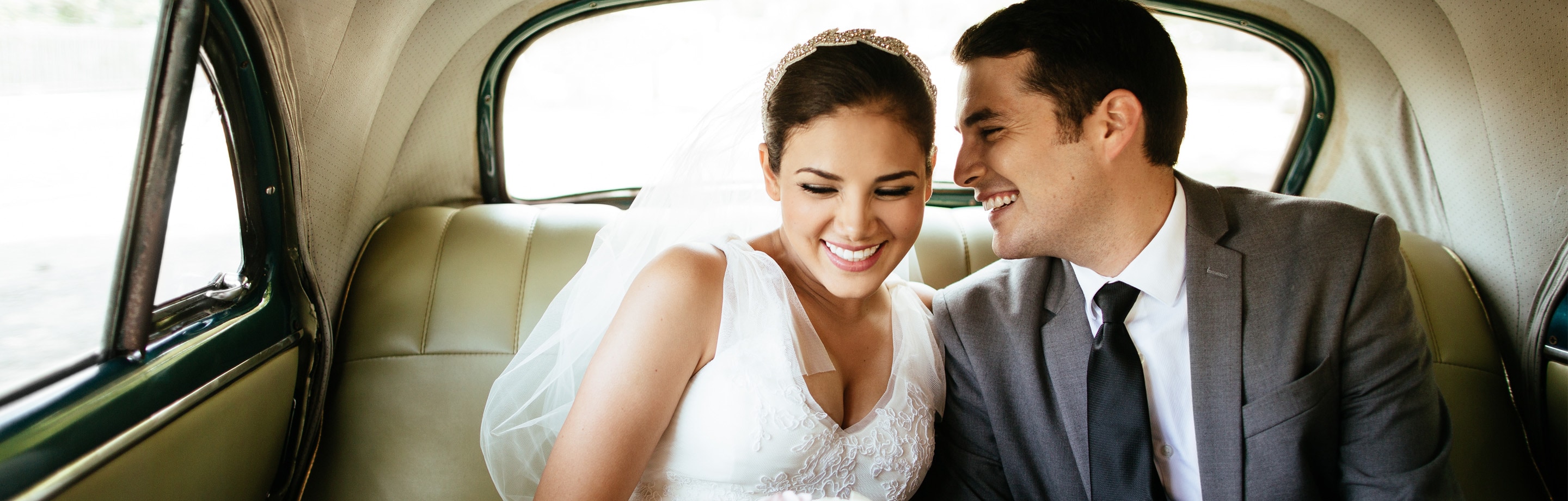 Happy newlywed Hispanic couple in car's back seat.