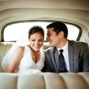 Young bride and groom smiling in the backseat of a classic car