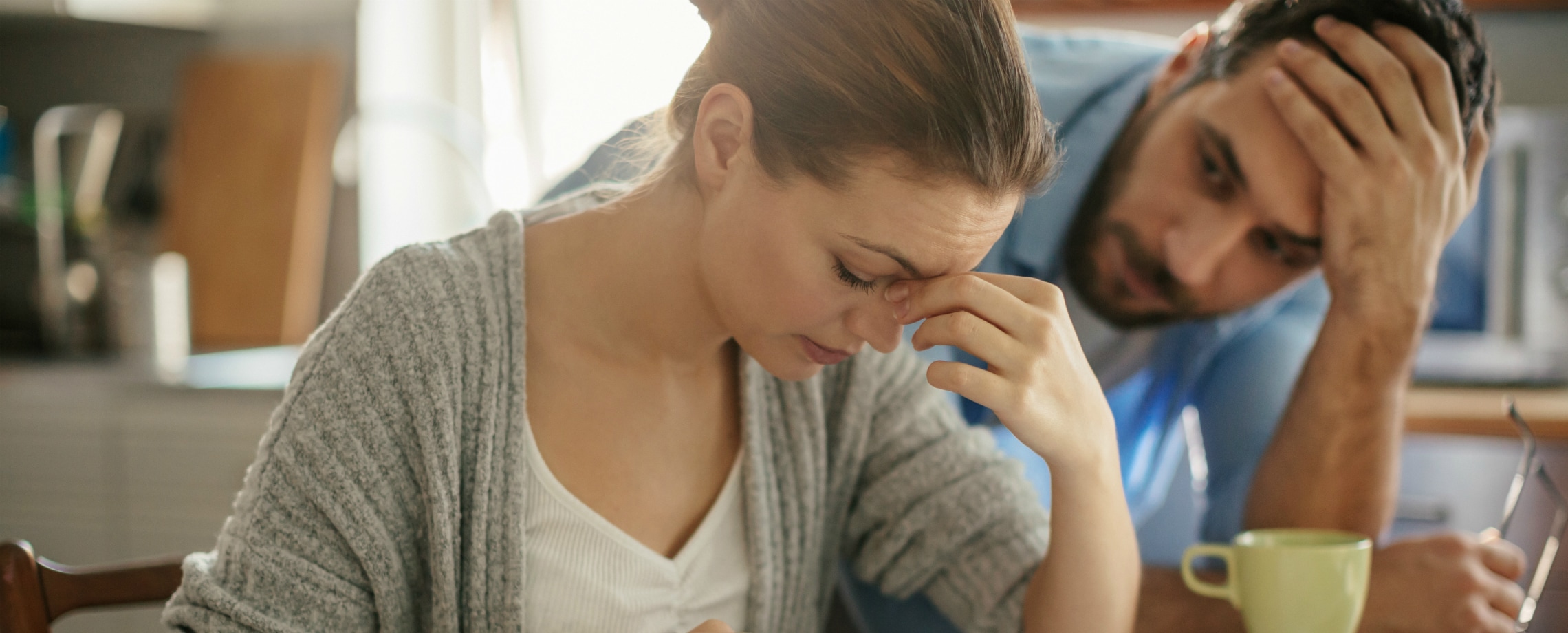 Close up of young couple in kitchen, appearing distressed by what woman is viewing on counter