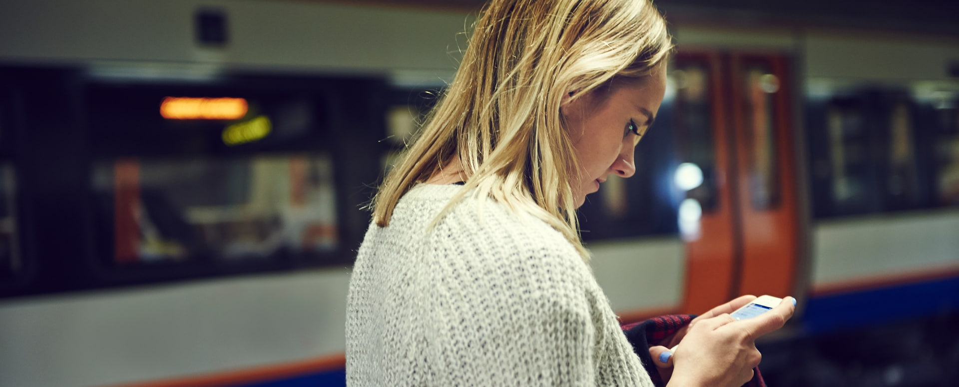 Blond woman by subway car looking at smartphone