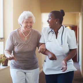 Older white haired Caucasian woman and African-American woman doctor walking arm-in-arm laughing