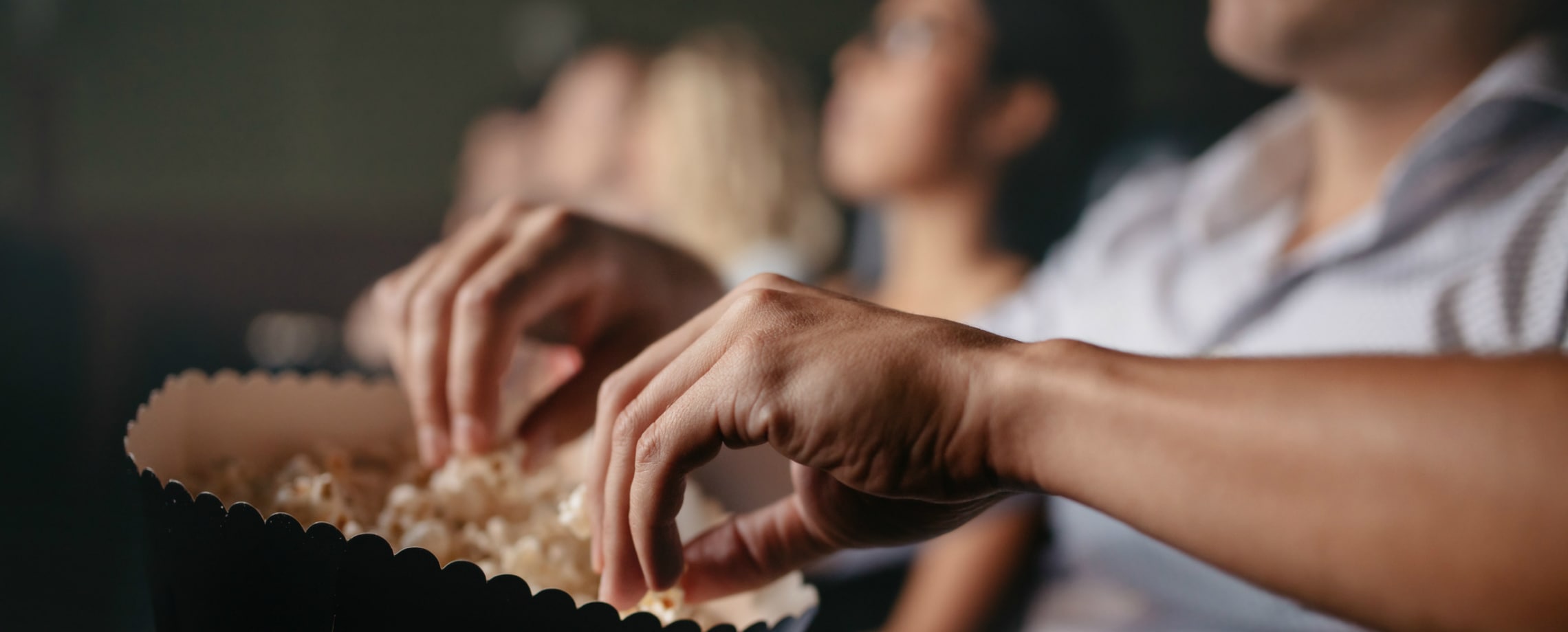 Close up of hands reaching into a bucket of popcorn at a movie