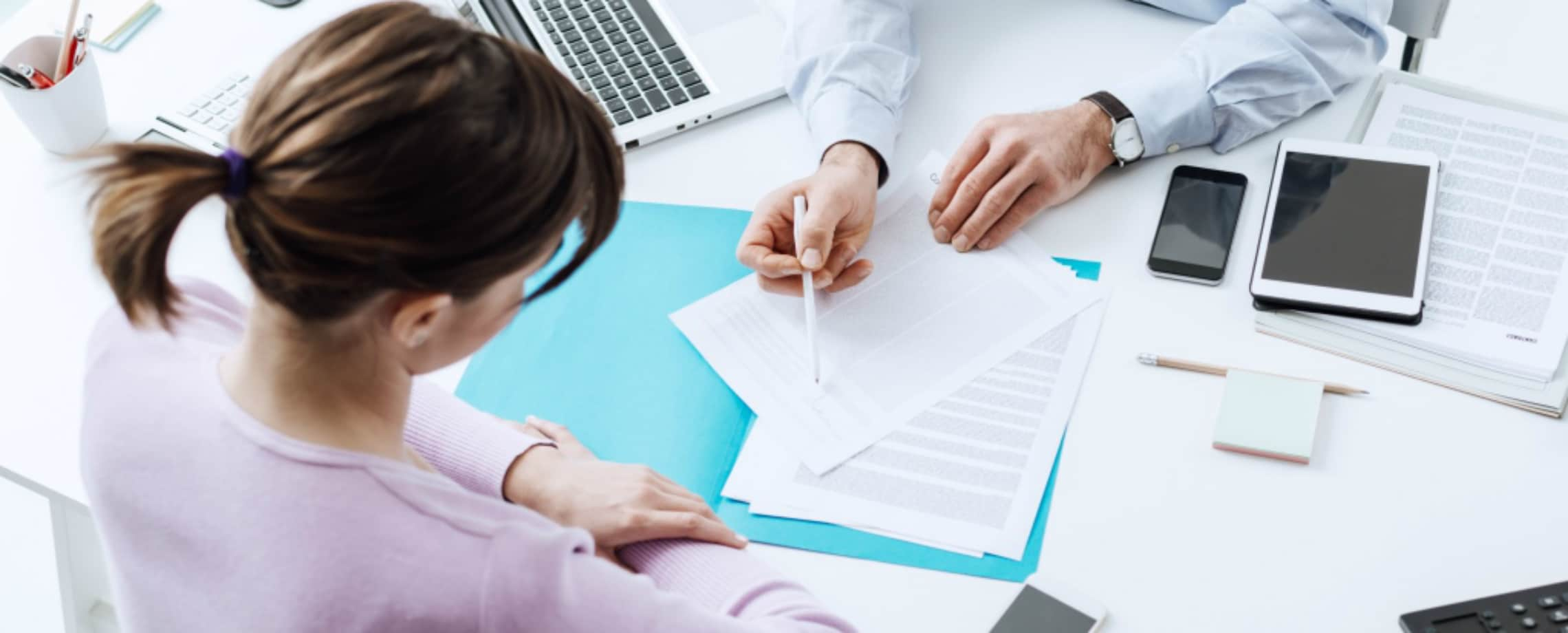 Arial view of man's hands pointing to female where to sign a document