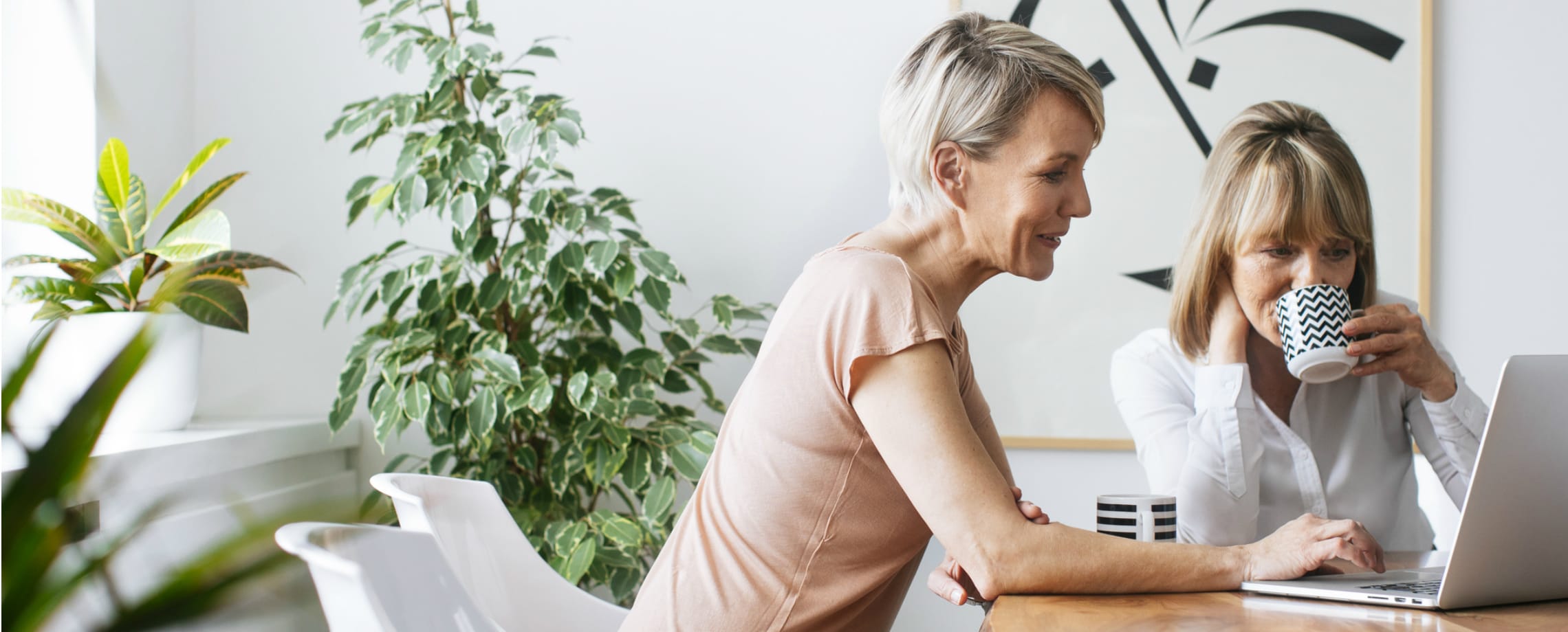 Two middle-aged Caucasian women at table with coffee and laptop