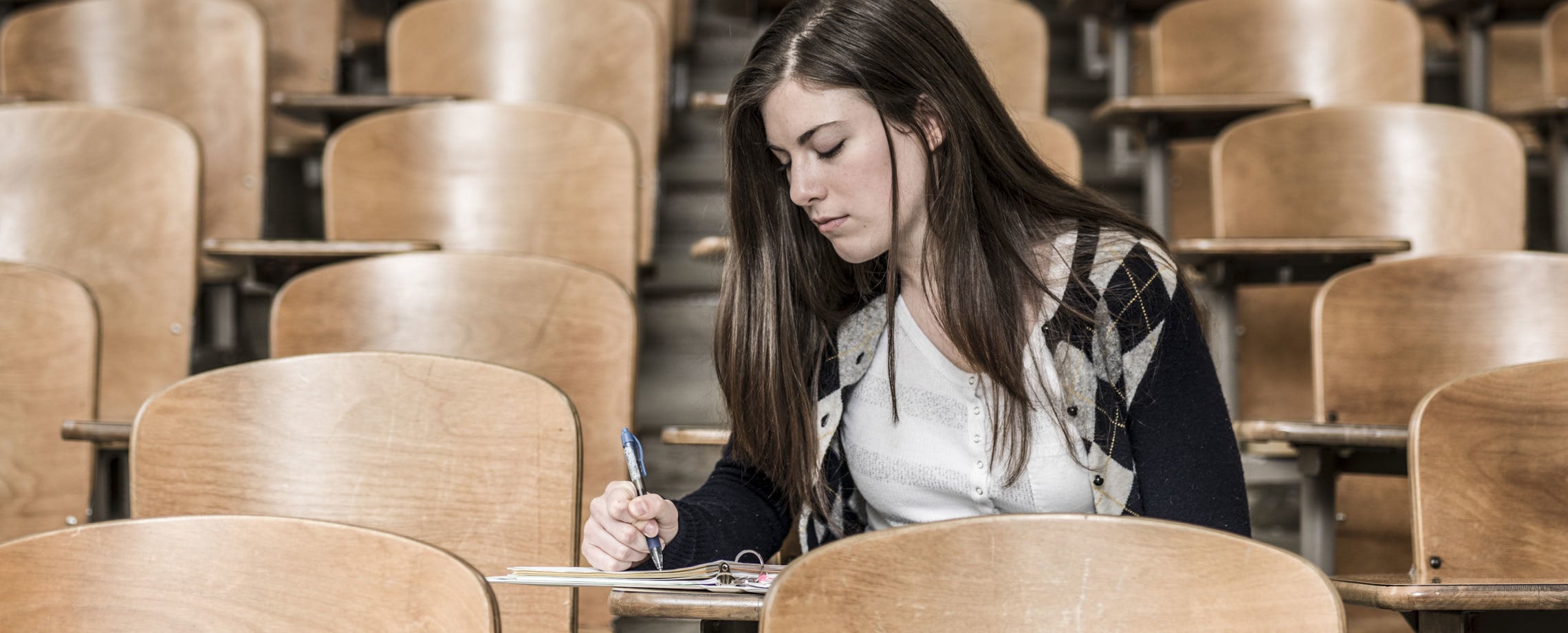 Young woman student taking notes in empty lecture hall