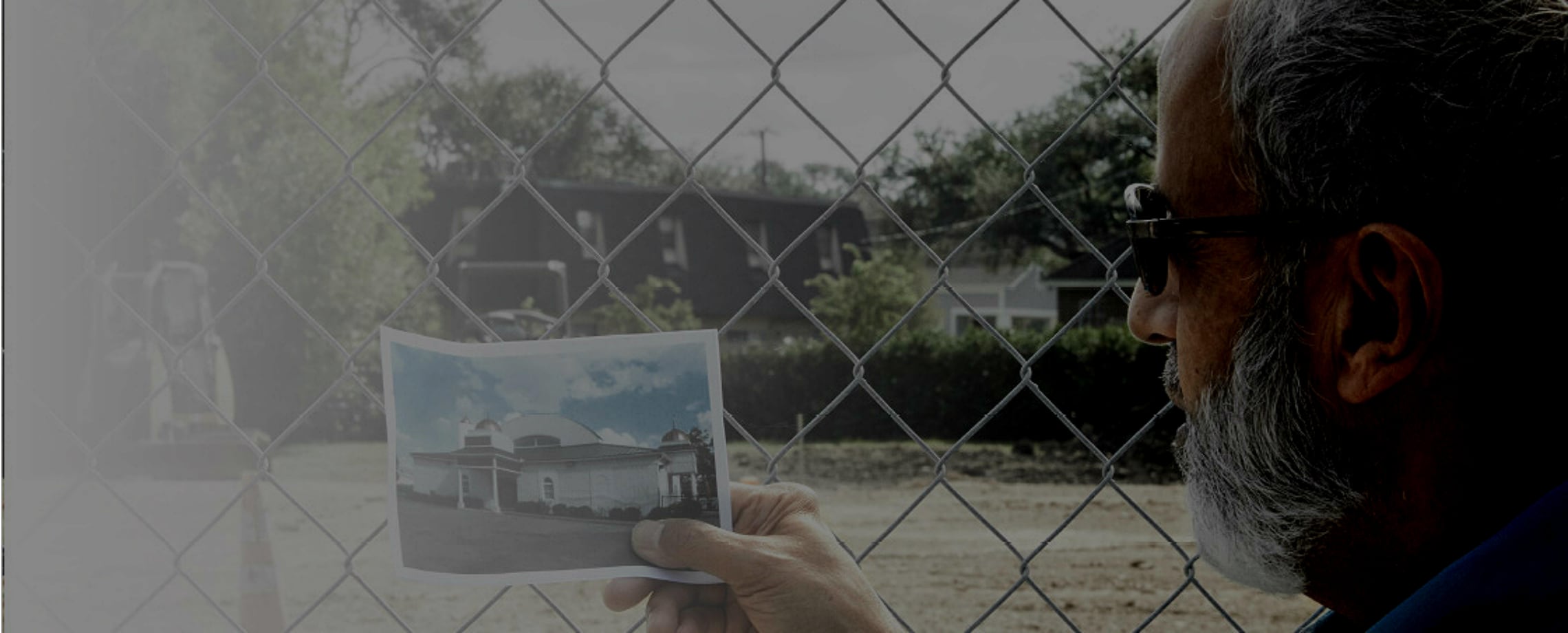 Man looking at vacant lot and holding a photo of a religious building that stood there
