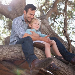 Father and young son sitting on thick tree branch