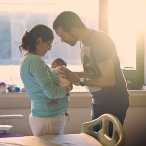 Mother and father standing, holding newborn in a hospital room