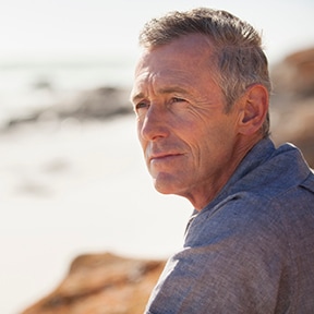 Man sitting by ocean and looking down the shore