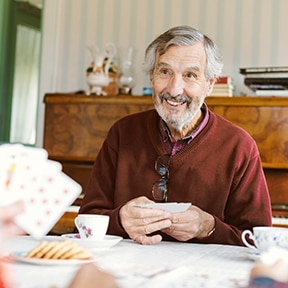 Retirement aged Caucasian man with beard sitting at table playing cards with others