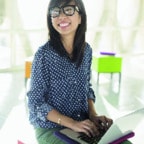 Young woman sitting in front of windows with laptop on lap