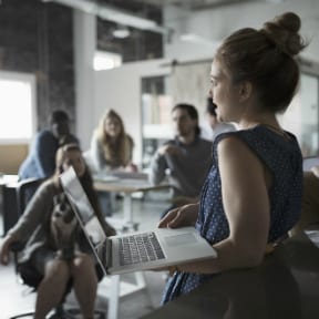 Woman with laptop speaking to group of young adult students