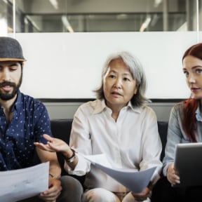Three people sitting with papers in hand with Asian woman asking a question