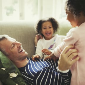 Caucasian man lying on couch playing with two African-American young girls