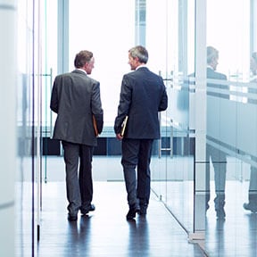 Two businessmen walking down an office hallway away from camera