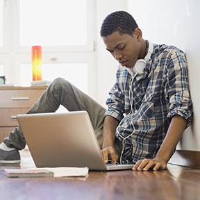 Young African-American man with headphones working on the floor with laptop