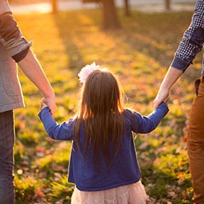 Young girl seen from the back between her moms and holding their hands