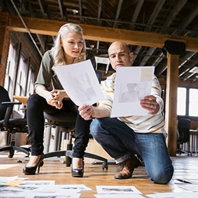 In professional warehouse workspace, coworkers reviewing documents spread out on floor