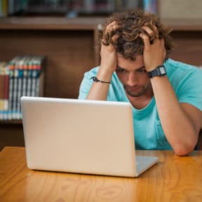 Frustrated looking Caucasian sitting man with hands on head looking at laptop