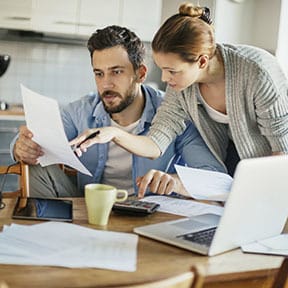 Young Caucasian couple reviewing finances on laptop at kitchen table