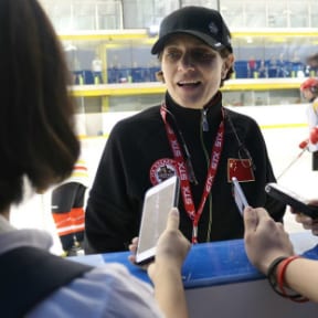 Woman with cap and lanyard giving a press conference at a hockey arena
