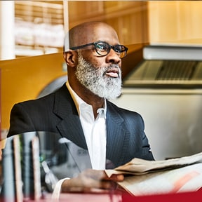 African-American businessman with shaved head and full beard reading newspaper at a table