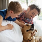 Boy and his father laying near edge of bed, patting dog on floor