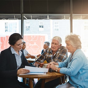 Middle aged Caucasian female in business suit going over documents with retirement aged Caucasian couple in a coffee shop