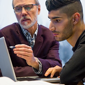 Older man reviewing something on a laptop with younger man of Middle Eastern descent
