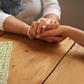 Close up of an older woman of color's hands holding those of a younger woman