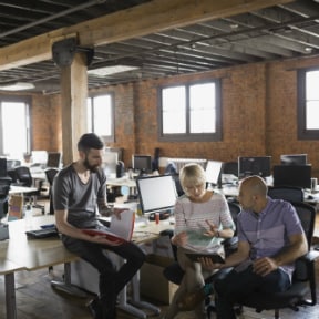 Three Multi-ethnic,  office workers sitting talking in a warehouse type office