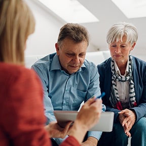 Older couple being shown something on a laptop by another woman