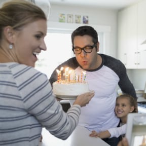 Man in glasses blowing out birthday candles with family nearby