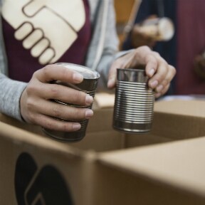 Close up of volunteer's hands putting canned goods in a box