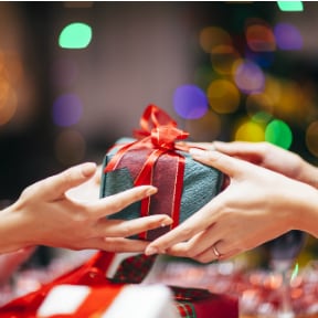 Close up of two women's hand exchanging and wrapped present with red bow