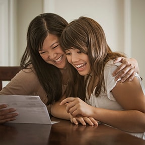 Asian-American mother and young adult daughter smiling at a letter together