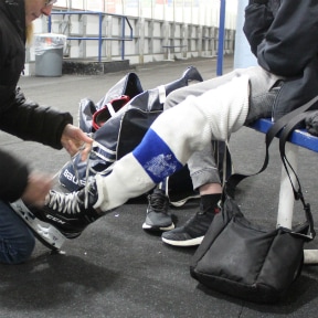 Close up of kneeling man helping to put on another person's skate