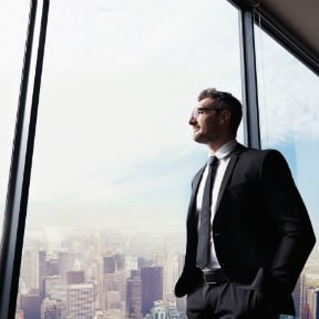 Businessman in suit standing at office window overlooking the city