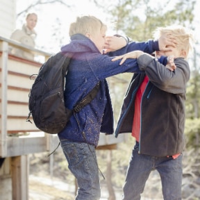 Two boys dressed for outside playfully fighting in their backyard