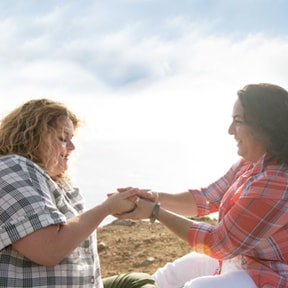 Two Caucasian females sitting on the ground holding hands and smiling