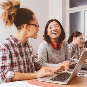 Multicultural group of women students working at computers smiling and talking