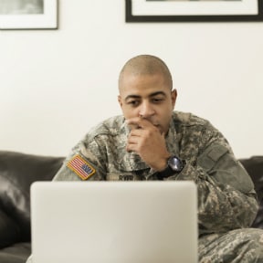 Young African-American uniformed U.S. Army soldier looking at a laptop in a living room