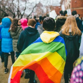 Group of young people marching, one draped in a rainbow flag
