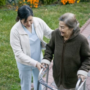 Asian woman nurse helping and older Asian woman with a walker