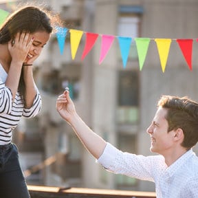 Young androgynous Caucasian person proposing to their girlfriend of color